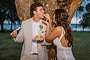 Boho bride in fringe dress cutting cake with groom in light beige suit