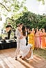 Boho bride in fringe dress dancing with groom in light beige suit surround by bridal party in mismatched dresses