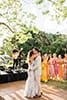Boho bride in fringe dress dancing with groom in light beige suit surround by bridal party in mismatched dresses